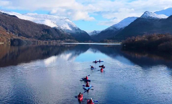 A group of kayakers paddling towards some snowy mountains